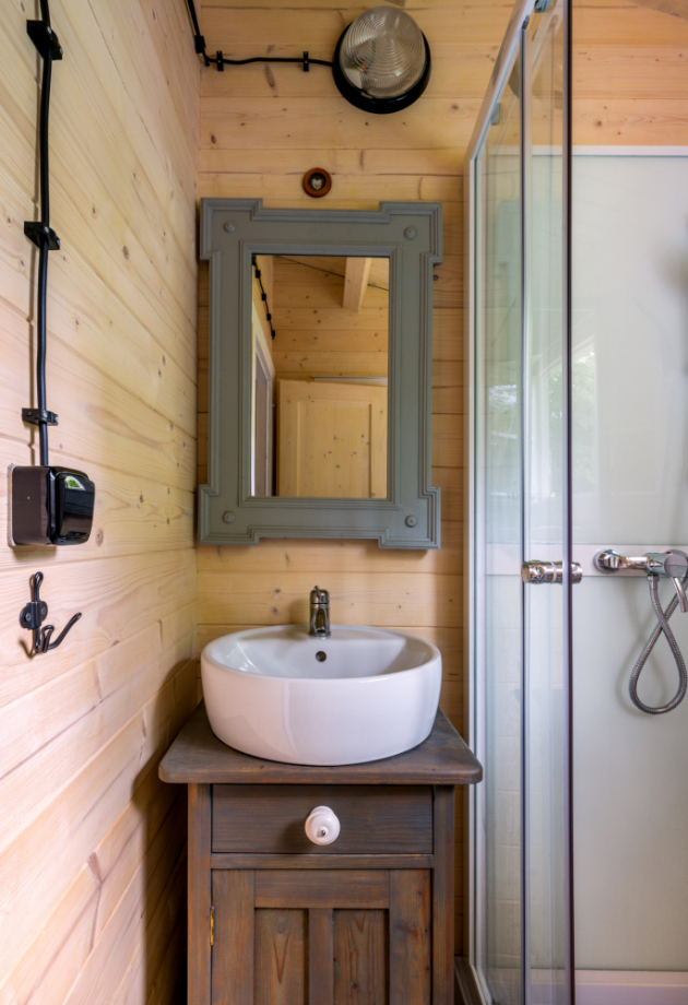 Do miniaturní koupelny se vešel sprchový kout, toaleta a umyvadlo posazené na nočním zrestaurovaném stolku. Zrcadlo má rám původem od popelnice