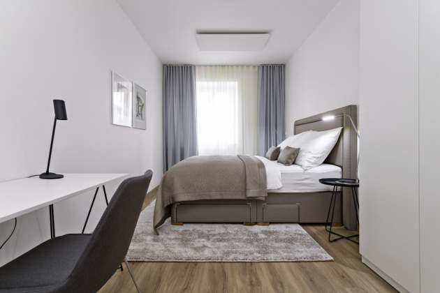 LOŽNICE Tlumené uklidňující barvy a komfortní postel od Ambience Design jsou hlavními prvky ložnice. Vešel se tam i minimalistický pracovní stůl a vysoká šatní skříň