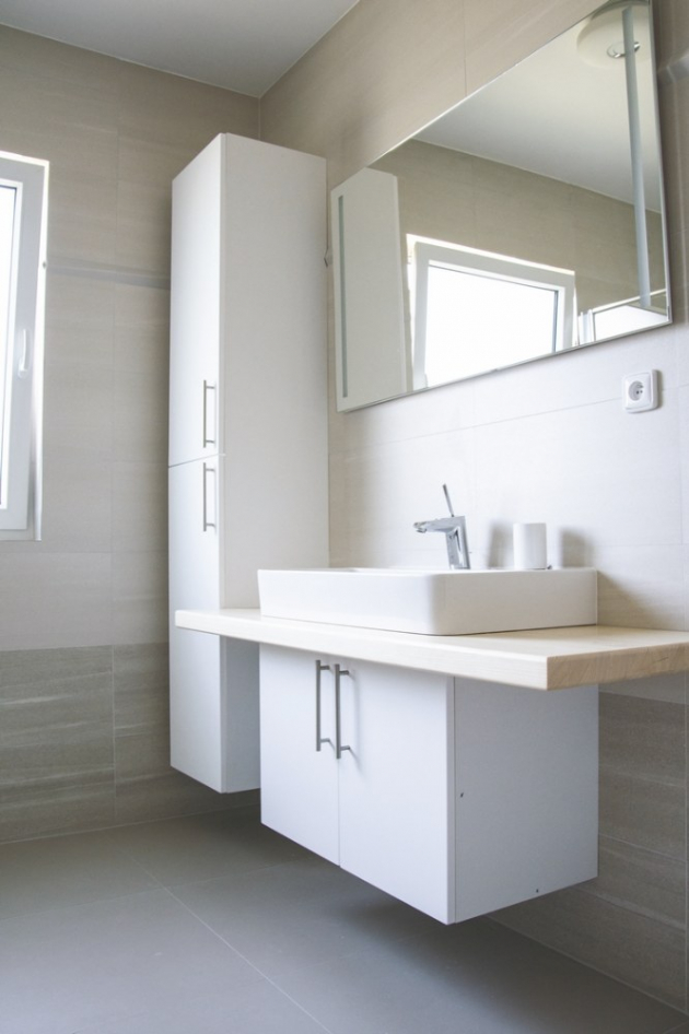 Koupelna s WC, jejíž obklady, dlažbu i sanitární zařízení si majitelé přáli vybrat sami, je taktéž laděna do bílých barev. Nábytková dvířka v kombinaci s přírodním dřevodekorem na desce pod umyvadlem a lehce šedá dlažba přechází v béžový kachlový obklad, čímž se místnost opticky zvětšuje.