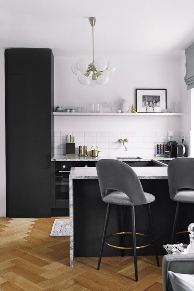 Černá velmi dobře vybavená kuchyň s mramorovou pracovní deskou a zlatými doplňky dodává bytu pocit luxusu