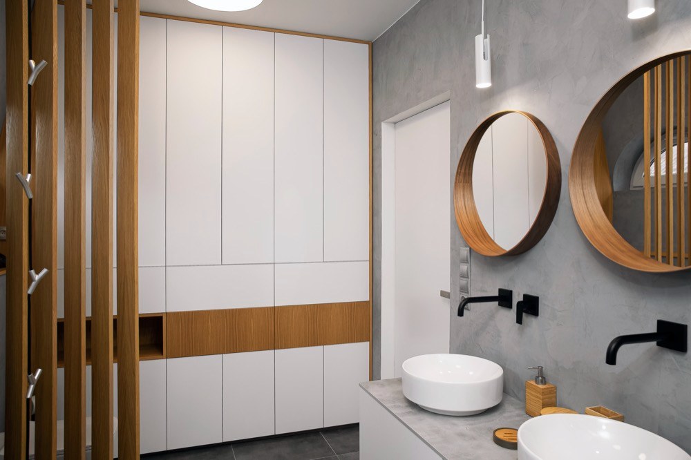 Základní barvou koupelny je šedá a její chlad potlačují zrcadla s dřevěným rámem a dřevěný paraván, který opticky odděluje toaletu od koupelny 