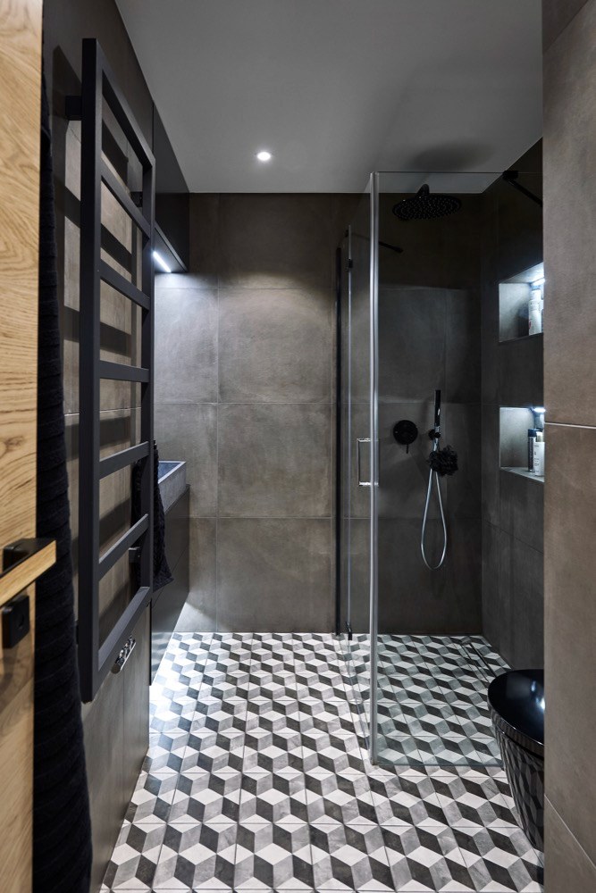 Prostor koupelny pohledově prosvětluje šedo-bílá retro dlažba, která je ve formě obkladů použita také nad umyvadlem a v nikách ve sprchovém koutu