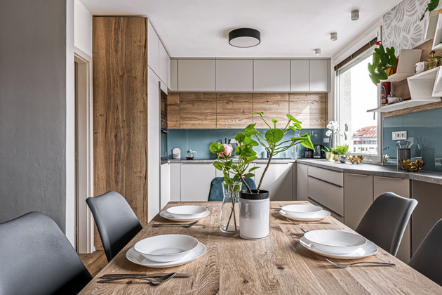 Kuchyňskou sestavu, s osvědčenou kombinací matné bílé s výrazným dekorem dubového dřeva oživuje lesklý modrozelený obklad stěny  nad pracovní plochou, www.jninterier.cz