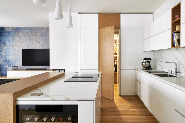 Kuchyň Elite, bílý lesklý lak a světlá dubová dýha použitá na dveřích do spíže, polici a části ostrůvku