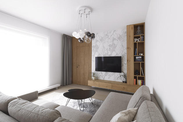Na první pohled v obývací místnosti zaujme mramorové obložení s dřevěným nábytkem v dubovém dekoru. Spojovacím prvkem celého bytu je svisle profrézovaný dřevěný obklad, který v sobě ukrývá dveřní křídlo